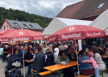 Gäste sitzen unter Schirmen vor dem Gerätehaus