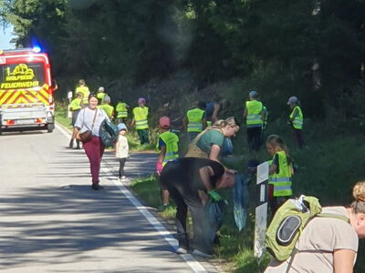 Mit leuchtgelben Warnwesten ausgestattete Kinder suchen im Gras nach Müll