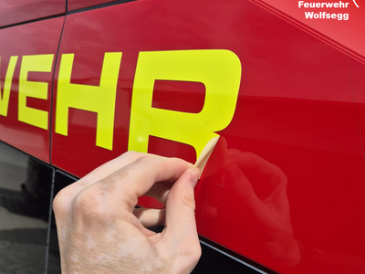 Ein Schriftzug wird auf einem Feuerwehrfahrzeug aufgebracht