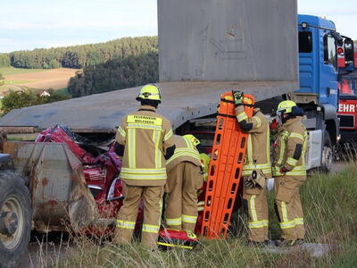 Bild zeigt ein eingeklemmtes Auto unter einem LKW, davor stehen Feuerwehraktive