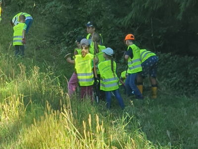Mit leuchtgelben Warnwesten ausgestattete Kinder suchen im Gras nach Müll