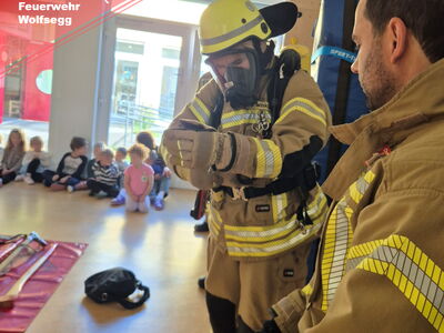 Zwei Feuerwehrmänner erklären Kindern ihren Anzug
