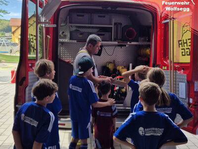 Ein aktiver Feuerwehrmann erklärt Kindern die Gerätschaften im Mannschaftswagen