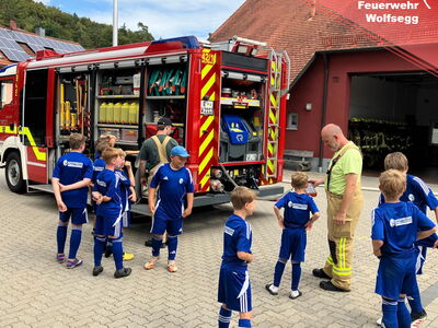 Kindern wird auf dem Platz des Gerätehauses das Feuerwehrauto erklärt
