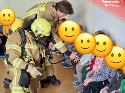 Zwei Feuerwehrmänner präsentieren Kindern ihre Gerätschaften