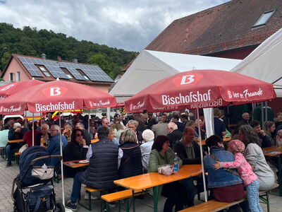 Gäste sitzen unter Schirmen vor dem Gerätehaus